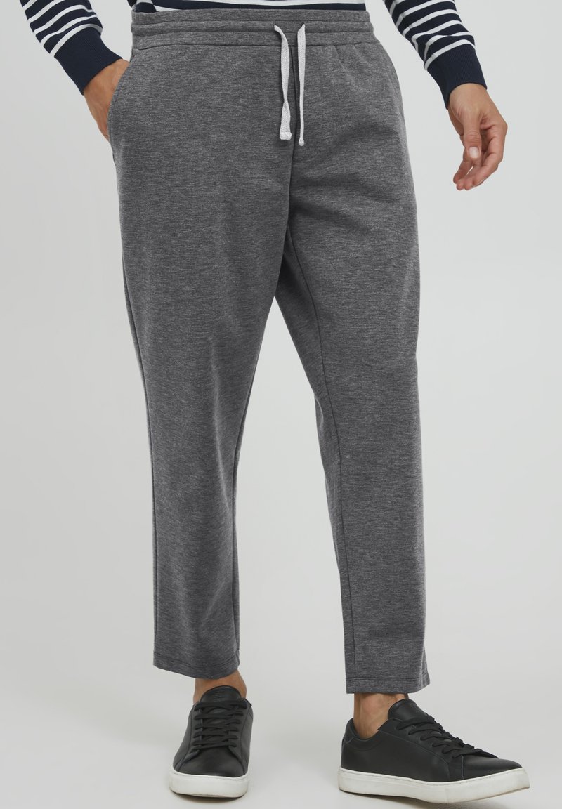 Graue Jogginghosen mit einem elastischen Bund und Kordelzug, Seitentaschen und schmal zulaufenden Beinen. Getragen mit schwarzen Turnschuhen.
