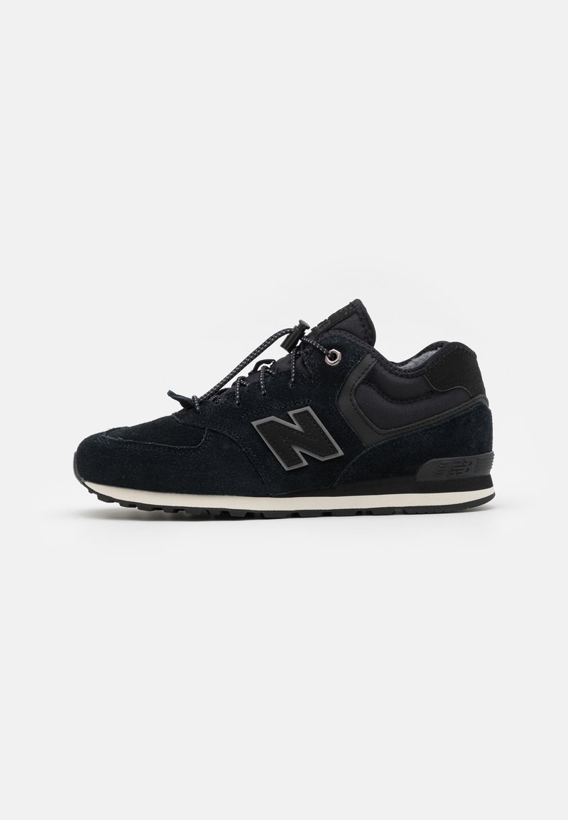 Chaussure de sport en suède noir et maille avec logo « N » réfléchissant, lacets élastiques à bouton de serrage et semelle rembourrée sur fond blanc.