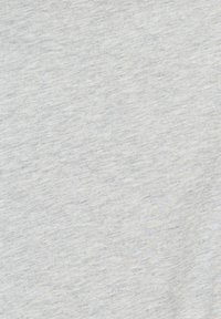 Femme en tenue de sport tenant des gants de boxe rouges, debout dans une salle de boxe avec des sacs et du matériel en arrière-plan.