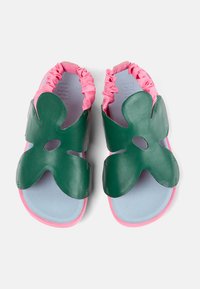 Gröna läder-sandaler med blomformade remmar, ljusblå fotbäddar, rosa elastiska ankelsnören och rosa sulor, sedd uppifrån.