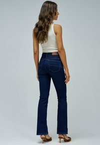 Vaqueros acampanados de un azul oscuro con una cintura alta y bolsillos traseros discretos, combinados con una blusa ajustada blanca y tacones marrones.