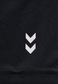 Zwarte stof met een gladde textuur, met een wit chevron-logoontwerp nabij de onderkant. Eenvoudige, minimalistische esthetiek.
