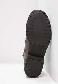 Hnědá kožená bota s texturovanou gumovou podrážkou. Podrážka má hluboké výstupky pro lepší přilnavost, zatímco svršek má ozdobné švy.