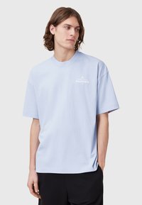Light blue cotton t-shirt with short sleeves, a round neck, and white logo text on the chest. Relaxed fit with a soft texture.