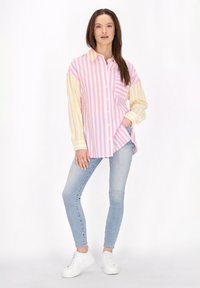 Camicia a righe nei toni del rosa e giallo con maniche lunghe, abbinata a jeans skinny blu e sneakers bianche.