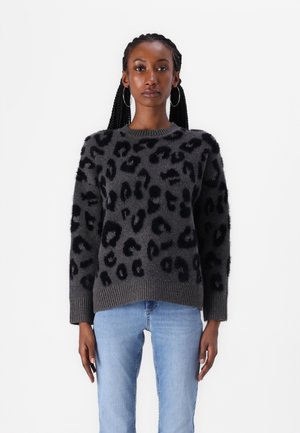 Un pull en laine moelleuse avec un motif léopard noir, base grise, encolure et poignets côtelés, associé à un jean bleu clair. Texture douce et coupe décontractée.