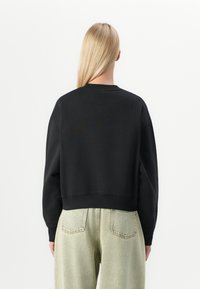Zwarte cropped sweatshirt met geribbelde ronde hals en lange mouwen, gecombineerd met lichtgroene high-waisted jeans met achterzakken.