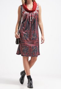 Makelaar met bloemenpatroon in donkere tinten met een rode kraag, voorzien van decoratieve stiksels en een uitlopende rok.