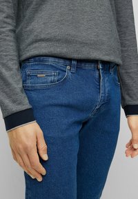 Mörkgrå långärmad skjorta med rundad halsringning som matchas med blå denimjeans. Jeansen har en framficka och en liten logotagg.