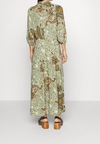 Abito lungo in tessuto verde chiaro con motivi floreali e paisley, dotato di colletto, maniche a tre quarti e dettagli con bottoni. Sandali con tacco a blocco.