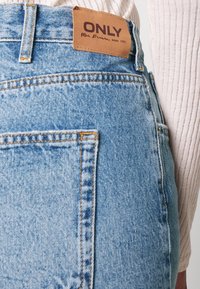 Shorts de mezclilla de tiro alto en azul claro con costuras naranjas, presentan una etiqueta de cuero marrón que dice "ONLY" y un bolsillo trasero.