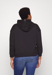 Sudadera recortada negra con capucha, que presenta un pequeño detalle en rojo, blanco y azul en la parte de atrás, combinada con jeans azules. Material de algodón.