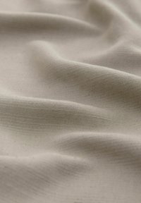 Beige audums ar gludu, nedaudz teksturētu virsmu, ar maigiem krokām un smalkām tonālo un ēnojuma variācijām.