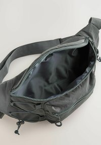 Borsa a vita grigia in tessuto con una tasca esterna con zip, cintura regolabile e fodera interna liscia. Presenta corde elastiche per ulteriore spazio di stoccaggio.
