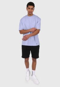 Lys lilla t-skjorte med kort erm, avslappet passform, kombinert med svarte shorts. Tilbehør inkluderer hvite klumpete sneakers og ankelstrømper.