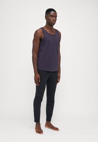 Débardeur violet foncé avec un col rond, associé à un jogger noir slim-fit. Le tissu semble lisse, sans motifs ni embellissements visibles.