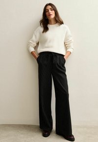 Suéter de gran tamaño en color crema con pu�ños acanalados, combinado con pantalones de pierna ancha a rayas negras y zapatos de plataforma. Textura suave y corte relajado.