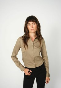 Hellebrauner, langärmeliger Hemd mit Knöpfen und strukturiertem Kragen, kombiniert mit schwarzen Hosen. Glatte Stofftextur.