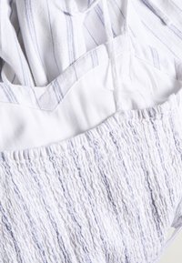 Textile avec une base blanche et des rayures verticales bleues, une texture smockée froncée et des bretelles fines. Tissu délicat et léger.