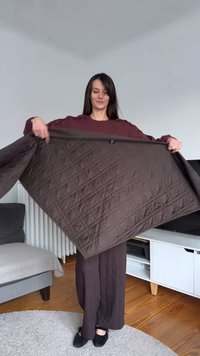 Brown quilted blanket held open, featuring a diamond pattern, smooth texture, and a small black tag. Soft material, displayed in a bright room.
