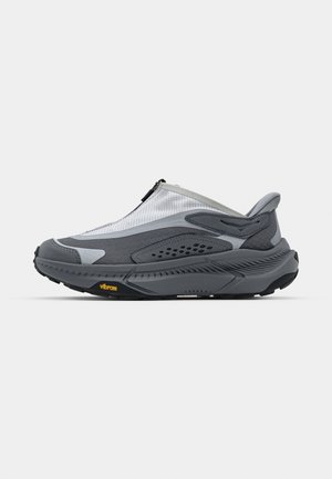 Grijze sportieve schoen met een bovenwerk van mesh, ritssluiting en getextureerde overlays. Voorzien van een Vibram-buitenzool voor grip en duurzaamheid.