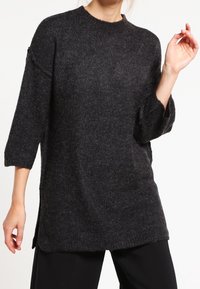 Pull tricot oversize gris foncé avec un col rond, des manches trois-quarts, des fentes latérales et une finition douce et texturée.