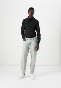 Camisa negra de botones, vaqueros de mezclilla azul claro y zapatillas blancas. La camisa tiene cuello y mangas largas; los vaqueros son de corte ligeramente holgado.
