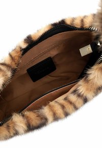 Somu iekšpuse ar brūnu auduma oderi, iekšējo rāvējslēdzēja kabatu, mazu melnu birku un atveri ar ādas apdari un melnu rāvējslēdzēju.