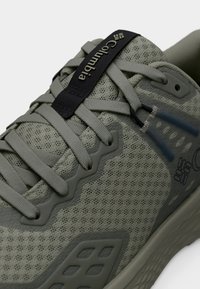 Γκρι αθλητικό παπούτσι με διαπνέον διχτυωτό υλικό και υφασματικές επικαλύψεις, επίπεδα κορδόνια και μαλακή σόλα. Διαθέτει λογότυπο σε σκούρο ταμπελάκι και αντιθετικές λεπτομέρειες.