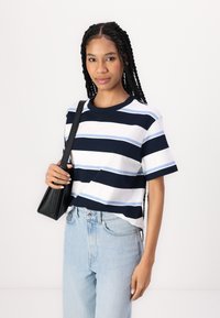 Navy and white striped t-shirt with light blue accents, short sleeves, a round neckline, paired with light denim jeans and a small black bag.
