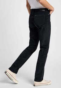 Svarta kordbyxor med rak bendesign, utrustade med bakfickor och en texturerad yta. Bärs med beige sneakers.