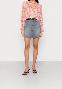 Blusa floreale rosa con maniche lunghe e scollatura a V, abbinata a una mini gonna di jeans grigia con orlo sfrangiato e sandali neri con tacco.