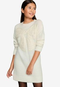 Hellbeiges gestricktes Kleid mit einem strukturierten, großen Schleifendekor auf der Vorderseite. Verfügt über gerippte Bündchen und einen gerippten Saum; weicher, flauschiger Stoff.