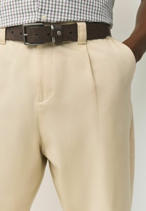 Beežid plisseeritud püksid valmistatud pehmest kangast, sobitatud tumedat pruunist nahkvööga, millel on hõbedane pandlaga ja küljetaskud.