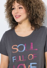 Donkergrijze katoenen t-shirt met kleurrijke, oversized tekst "SOUL FULL OF LOVE" in oranje, blauw en roze tinten. Korte mouwen, ronde hals.