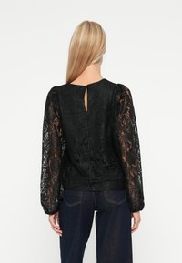 Czarna koronkowa bluzka z długimi, bufiastymi rękawami, zapięciem na plecach w kształcie łezki oraz dopasowanym pasem. Tekstura jest skomplikowana z kwiatowymi wzorami.