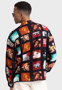 Kolorowa koszula zapinana na guziki, z mieszanką przerośniętych obrazów sztuki pop i tekstu na czarnym tle, z długimi rękawami i luźnym krojem.