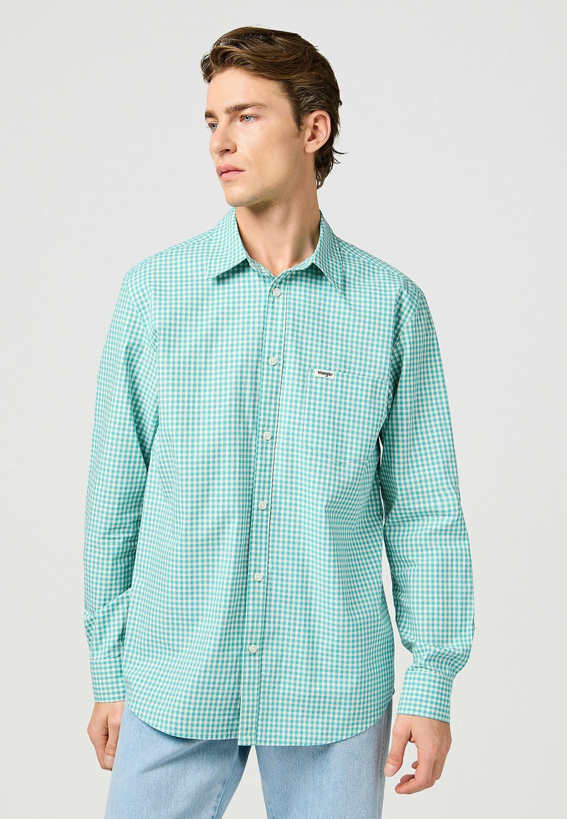 Camisa de cuadros verdes de botón, con cuello, mangas largas y un solo bolsillo en el pecho. Hecha de una tela ligera con una textura suave.