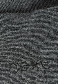 Tissu gris foncé avec une texture tissée. Comprend du texte imprimé discret, possiblement un nom de marque, aligné horizontalement dans une police simple.