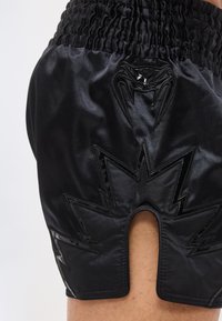 Μαύρο σατέν σορτς με ελαστική μέση, που διαθέτει γυαλιστερό σήμα νυχτερίδας πάνω από μια σχεδίαση με ζιγκ-ζαγκ αστραπή και κεντρική πίσω σχισμή.