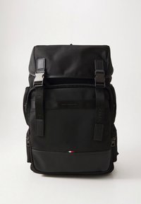 Melnā mugursoma no teksturētas auduma ar regulējamām siksnām, metāla aizdares, priekšējām kabatām un nelielu trīskrāsu akcentu apakšā.