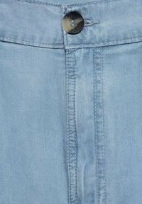 Svetlo modra denim tkanina ima sprednji zadrgo in črno gumbasto zaklepanje, z vidnimi šivi na šivih. Gladka tekstura.