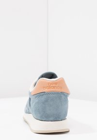Niebieskie zamszowe sneakersy z skórzanym akcentem. Posiadają zaokrąglony czubek i kontrastowy różowy uchwyt na pięcie wytłoczony napisem "new balance". Kremowa podeszwa.