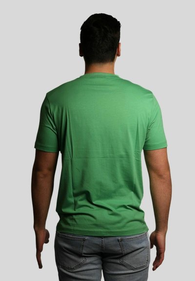 T-shirt in cotone verde con collo rotondo, maniche corte e una trama liscia, abbinata a jeans azzurri, vista da dietro.