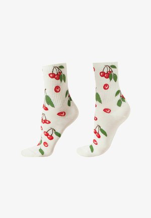 Białe skarpetki do kostki z czerwonym wzorem czereśni i zielonym liściem na prążkowanej tkaninie, pokazane z boku.