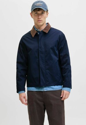 Chaqueta azul marino con un cuello de pana marrón, fabricada en material ligero. Presenta un cierre de botones y dos bolsillos laterales.