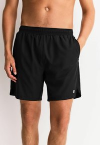 Schwarze Badeshorts mit elastischem Bund, Seitentaschen und kleinem Logodetail. Glatter Stoff mit lockerem, sportlichem Schnitt.
