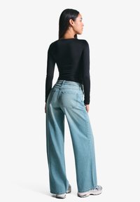 Černý top s dlouhým rukávem; světle modré široké džíny s dvěma zadními kapsami; model se otočený zády; bílé a černé tenisky.