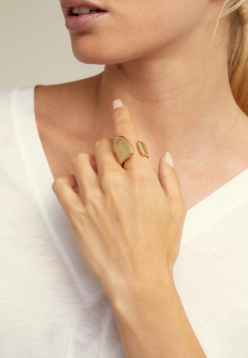 Conjunto de anillos de oro que presenta dos formas orgánicas: una más grande y lisa, y la otra más pequeña y con textura. Llevado en una mano sobre un fondo de tela clara.