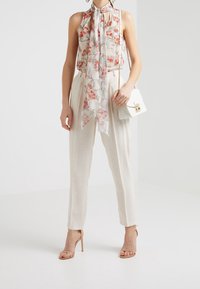 Kwiatowa bluzka bez rękawów z wiązanym dekoltem, lekki materiał. Kremowe szerokie spodnie, cieliste szpilki i mała biała torebka na klapkę.